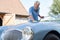 Mature Man Polishing Restored Classic Sports Car Outdoors At Home