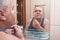 Mature man shaves in bathroom in morning, reflection in mirror portrait