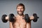 Mature man shirtless standing with dumbbells smiling