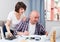 Mature man sitting with documents and laptop, wife trying helping