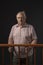 Mature man in sixties on trial, standing behind wooden dock, black background