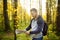 Mature man tourist is hiking. Person looking map during orienteering in sunny autumn forest. Volunteer is searching for people