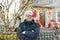 Mature man wearing Santa hat stand near his decorated home. Owner decorated his house and yard with garlands for Christmas and New