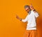 Mature man in white hoodie, pants and sunglasses, bracelets. Raised his forefingers up, posing on orange background. Close up