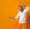 Mature man in white hoodie, pants and sunglasses, bracelets. Raised his forefingers up, posing on orange background. Close up