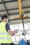Mature manual worker with digital tablet operating crane to lift steel in industry