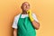 Mature middle east man wearing cleaner apron and gloves serious face thinking about question with hand on chin, thoughtful about