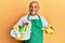 Mature middle east man wearing cleaner apron holding cleaning products smiling happy pointing with hand and finger
