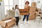 Mature mother and down syndrome daughter moving to a new home, standing by cardboard boxes holding welcome door mat