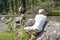 Mature photographer man taking photos of a blonde middle-aged model near a stream