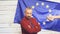 Mature politician in suit standing on stage in light against EU flag and ganswers questions from journalists with a