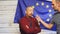 Mature politician in suit standing on stage in light against EU flag and ganswers questions from journalists with a