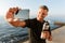 Mature sportsman take a selfie with bottle of water on the beach.