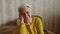 Mature white-haired European woman in yellow knitted sweater sitting, look at the camera medium closeup home background