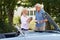 Mature Woman Bringing Hot Drink To Man Restoring Classic Sports Car Working On Engine Under Hood