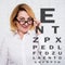 Mature woman in eyeglasses and eyevision test chart over white wall
