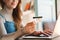 Mature woman in eyeglasses holding credit card while using on laptop in bright room