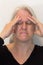 Mature woman with fingers to forehead, headache pain, eyes closed, neutral background
