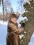 Mature woman in a fur coat stands leaning against a tree in a winter park