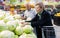 Mature woman with glasses picks a head of cabbage in vegetable section of supermarket