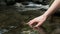 Mature woman hands touching and wetting the water of a lake in the mountain.