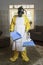 Mature woman in Haz Mat suit in living room with broom