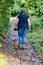 Mature woman with her dachshund seen from behind, standing looking down at a path with wet stones