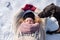 Mature woman in her fifties with red curly hair lies in the snow with gloves, hat and scarf and a dog licks her face with its