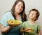 Mature woman holding salad and little cute boy with hamburger teasing close up, family food