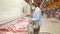 Mature woman in a mask and plastic gloves puts a pack of chilled meat in a supermarket trolley. Visiting the mall during