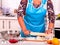 Mature woman pensioner knead dough at kitchen