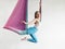 Mature woman pose in hammock performing aerial yoga or flying yoga exercise against white wall background in yoga studio room.