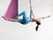 Mature woman pose in hammock performing aerial yoga or flying yoga exercise against white wall background in yoga studio room.