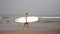 Mature woman senior citizen is walking along the beach with a surfboard.