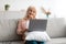 Mature woman sitting on couch and working on computer