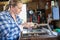 Mature Woman Upcycling Furniture In Workshop At Home Rubbing Down Cabinet With Sandpaper