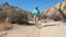 Mature Woman Walking In Dry Sandy Hot Desert With Huge Rocks Hills Bushes Cacti