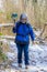 Mature woman walking on a frozen dirt trail surrounded by wild vegetation and snow with her mobile phone gimbal in hand