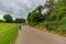 Mature woman walking with her dog on a paved path surrounded by farmland, trees and greenery with green foliage