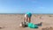 Mature woman with white hat and green gloves folding a large nylon picked up on the beach and put it in a garbage bag.