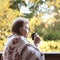 Mature woman in woolen plaid drinking hot beverage on the terrace looking at the autumn landscape. Fall mood concept. Copy space.