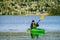 Mature women in green safety life jacket kayaking in green kayak, she looks at camera. Front side photo on still water