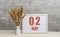 may 2. 2th day of month, calendar date. White vase with ikebana and photo frame with numbers on desktop, opposite brick