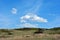 Meadow with green grass, hills with bushes, cloudy sky