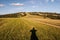 Meadow with pathway, photographer shadow, hill on the background and blue sky with clouds