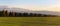 Meadow with small forest and hunters wooden high stand on autumn evening, some mountains in distance