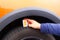 Measuring profile in hand. Tread depth meter at tire in orange car. Man is measuring the tread depth of his car tire