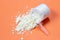 Measuring spoon with scattered protein powder, side view on a orange background