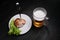 Meat with a fork stuck in it and a mug of beer on a dark wooden background