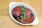 Meat marinating: Beef steak eye fillet in white dish of soy sauce marinade and rosemary herb sprig on wooden background -